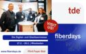 tde announcement as an exhibitor with their own booth at fiberdays 24 in Wiesbaden, Germany: in the foreground four employees standing around a trade fair counter, in the background trade fair wall with two product pics tML24+ and MMC connectors